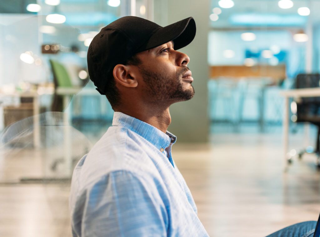 Side view of African American man marketer watching graphs on laptop screen while sitting with crossed legs on floor